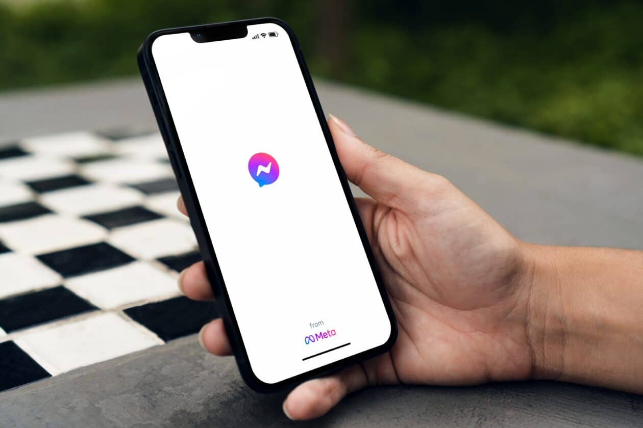 Mão segurando um iPhone com o Facebook Messenger abrindo