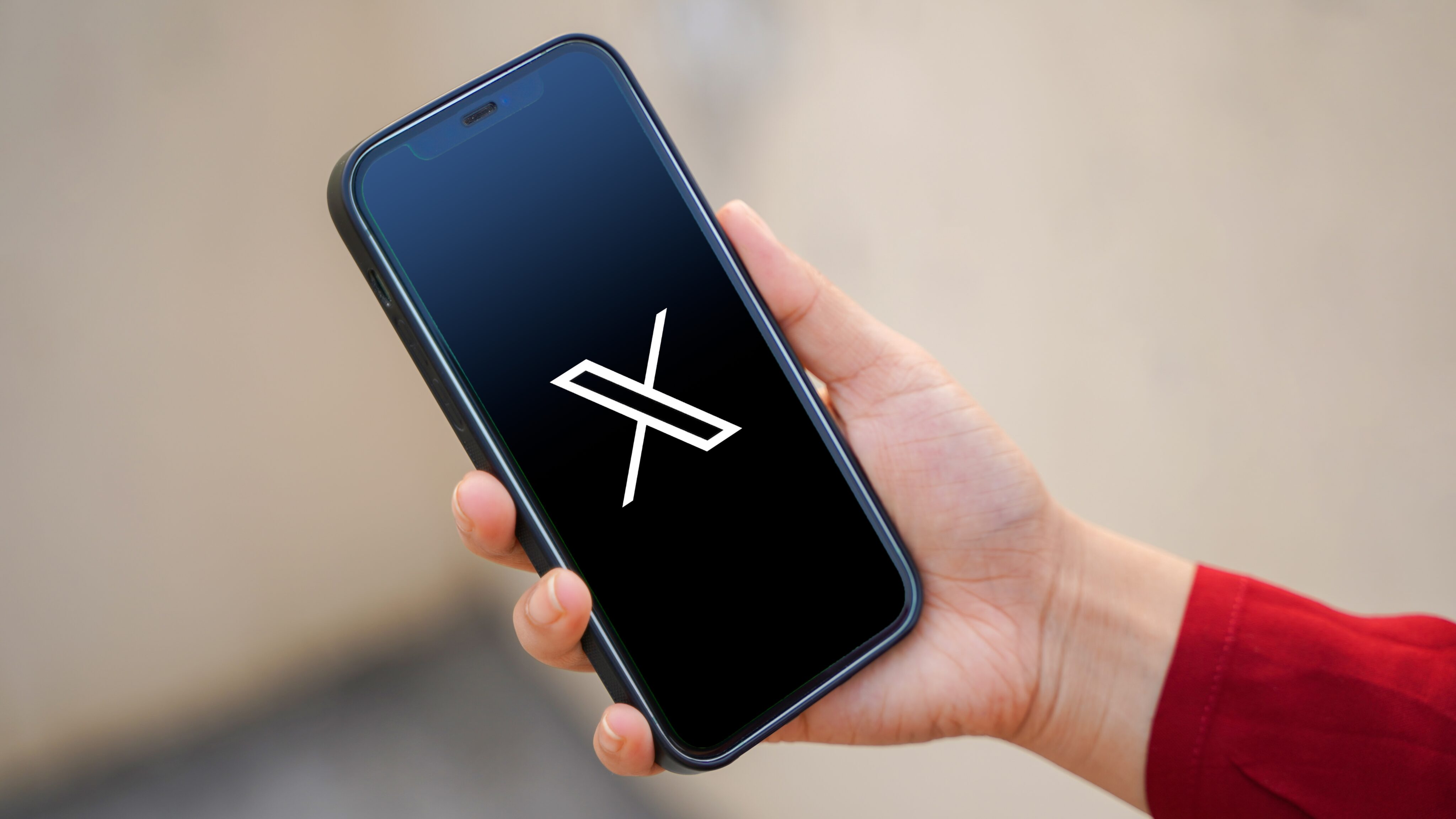 Mão segurando um iPhone com o logo do X